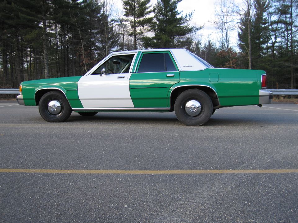 Green and white Ford sedan in side profile parked on paved lot