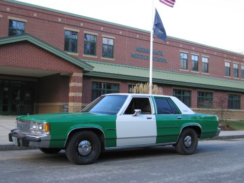 1991 Ford LTD Crown Victoria - green-and-white full-size Ford sedan parked at the curb in front of a brick building marked Merrimack Middle School.
