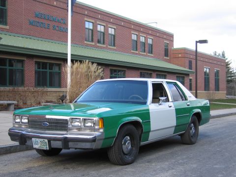 1991 Ford LTD Crown Victoria - Front three-quarter view of a green-and-white full-size Ford sedan with Ford grille emblem and a New Hampshire plate, outside a brick schoo…
