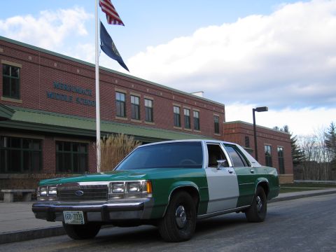 1991 Ford LTD Crown Victoria - green-and-white full-size Ford sedan parked along a brick middle school building beneath a partly cloudy sky.