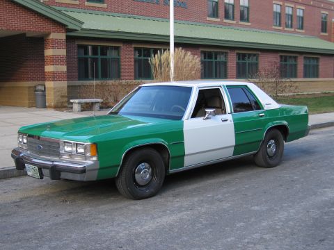 1991 Ford LTD Crown Victoria - Front three-quarter view of a green-and-white full-size Ford sedan with Ford grille emblem parked beside a brick building.