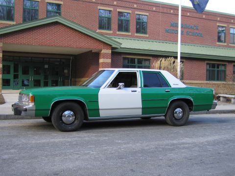 1991 Ford LTD Crown Victoria - Side profile of a green-and-white full-size Ford sedan parked in front of a brick building marked Merrimack Middle School.