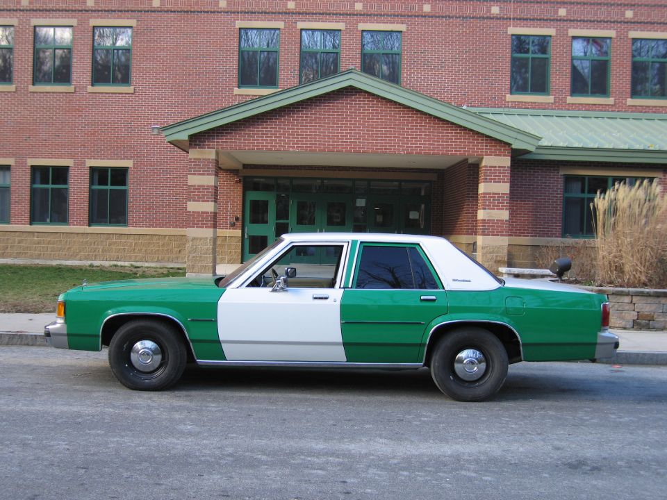 Green and white Ford sedan in profile by brick building entrance