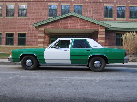1991 Ford LTD Crown Victoria - Side view of a green-and-white full-size Ford sedan parked along a brick building with a gabled entrance.