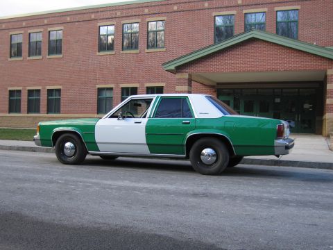 1991 Ford LTD Crown Victoria - Rear three-quarter view of a green-and-white full-size Ford sedan parked along a brick building.