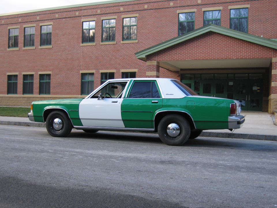 Green and white Ford sedan, rear three-quarter view, outside brick building