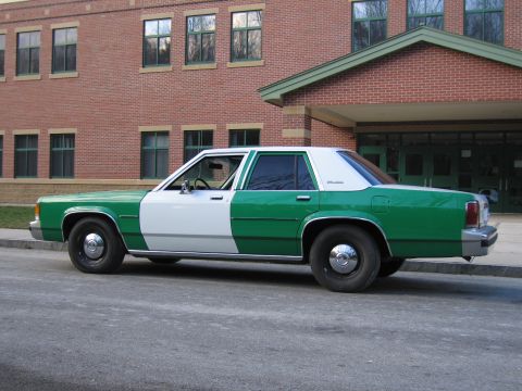 1991 Ford LTD Crown Victoria - Side profile of a green-and-white full-size Ford sedan parked at the curb in front of a brick building.