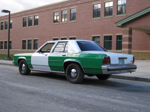1991 Ford LTD Crown Victoria - Rear three-quarter view of a green-and-white full-size Ford sedan with Ford trunk emblem parked along a brick building.