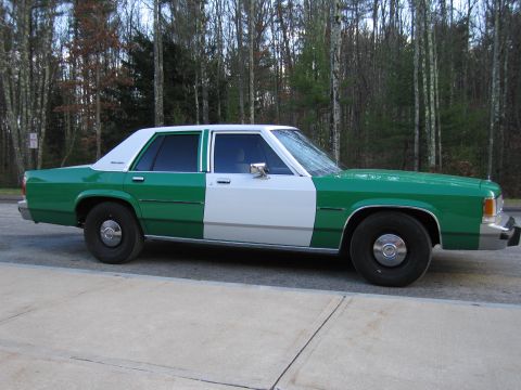 1991 Ford LTD Crown Victoria - Full driver-side profile of a green-and-white two-tone Ford four-door sedan parked on pavement among leafless trees.