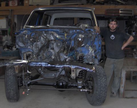 1990 Ford Bronco - Man stands with a 1990 Ford Bronco undergoing body re-installation, showing the disassembled front end.