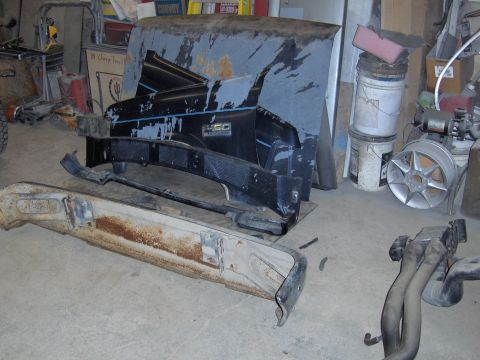1990 Ford Bronco - A disassembled black Ford F-150 fender with a blue stripe and a rusty bumper lie on a garage floor.