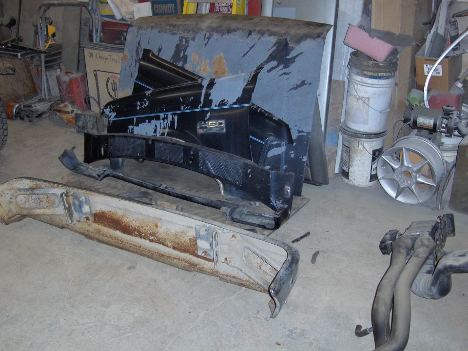 Black F-150 fender, rusty white bumper, and primer panels in a garage