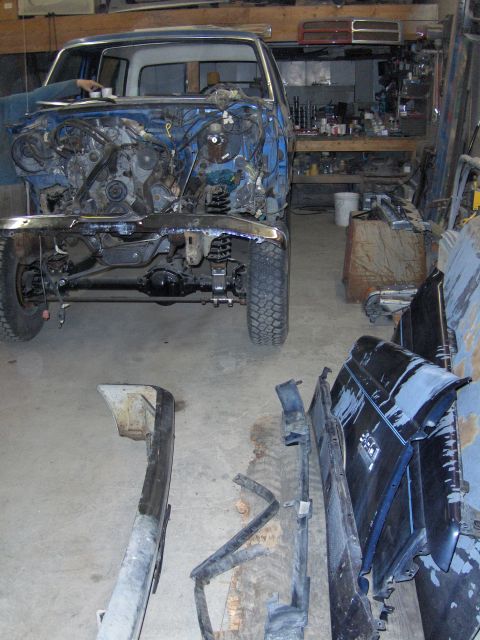 1990 Ford Bronco - A blue truck is disassembled in a workshop, with its engine exposed and various body parts laid out on the floor.
