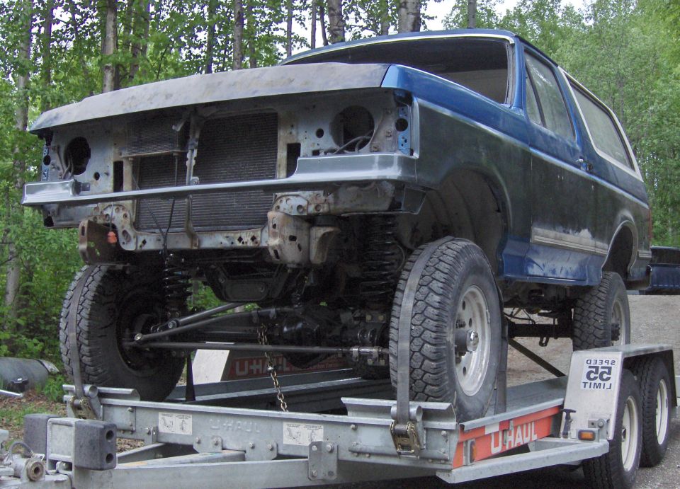 Blue Ford Bronco with front end stripped, on a U-Haul trailer outdoors