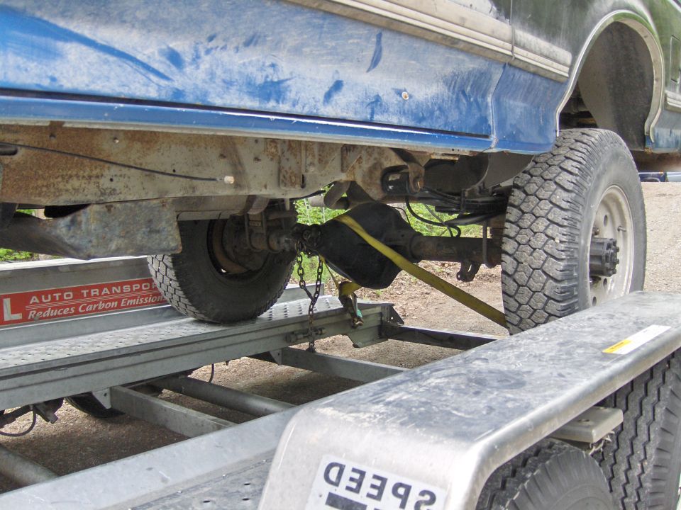 Blue Bronco undercarriage and rear axle strapped onto a silver transport trailer