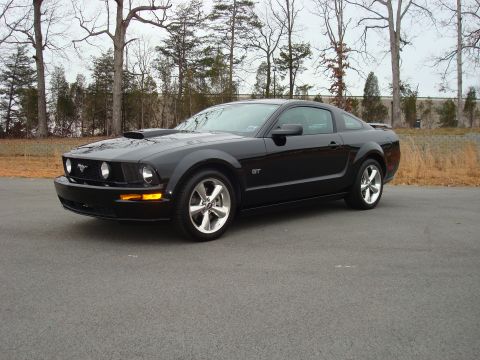 2007 Ford Mustang - A black 2007 Ford Mustang GT is parked outdoors on a paved surface with trees in the background.