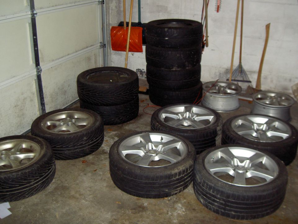 Several tires stacked up, with four sets of rims and tires in the foreground