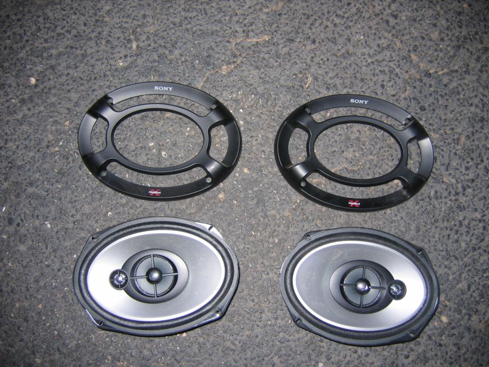 Two oval car speakers and two Sony speaker grilles on asphalt