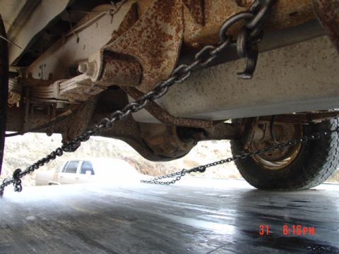 1979 Ford Bronco - Chains are attached to the undercarriage of a vehicle, with another vehicle in the distance.