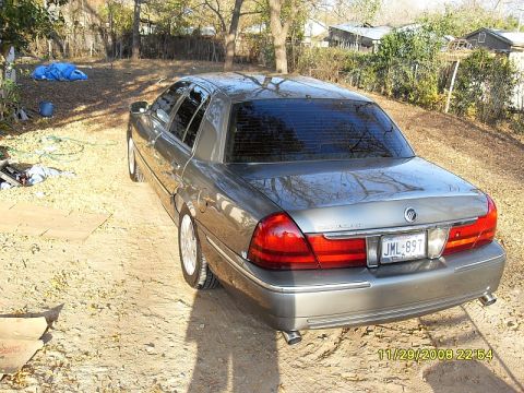 2004 Mercury Marquis - A gray 2004 Mercury Grand Marquis is parked in a dirt lot with trees and houses in the background.