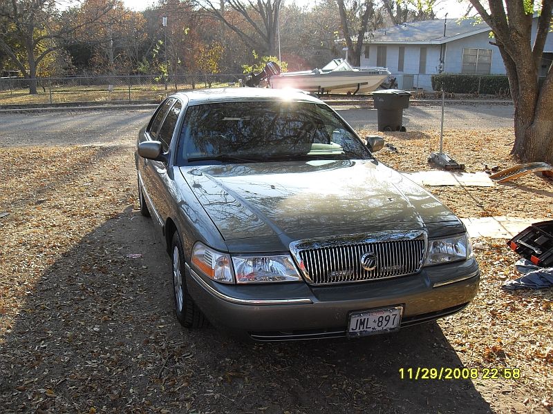 Gray Mercury Grand Marquis with chrome grille and license plate JML-897 parked on gravel