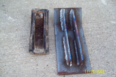 1900 Ford Wagon - Two metal parts, one rusty and one freshly welded, sit on a concrete surface.