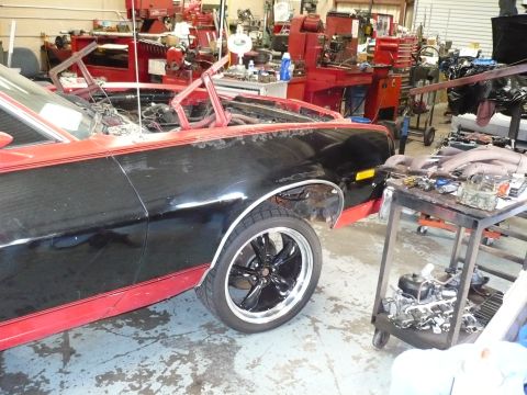 1973 Ford Ranchero - A black and red pickup truck, possibly from the early 1970s, is in a workshop with its hood open.