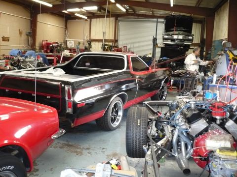 1973 Ford Ranchero - A black and red Ford Ranchero is parked in a workshop next to a red car and various engine components.