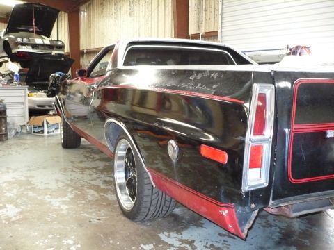 1973 Ford Ranchero - A black 1972 Ford Ranchero with red accents is parked in a garage, with another vehicle raised on a lift in the background.
