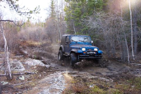 1991 Jeep Wrangler - A blue Jeep Wrangler navigates a muddy path in a forest environment.
