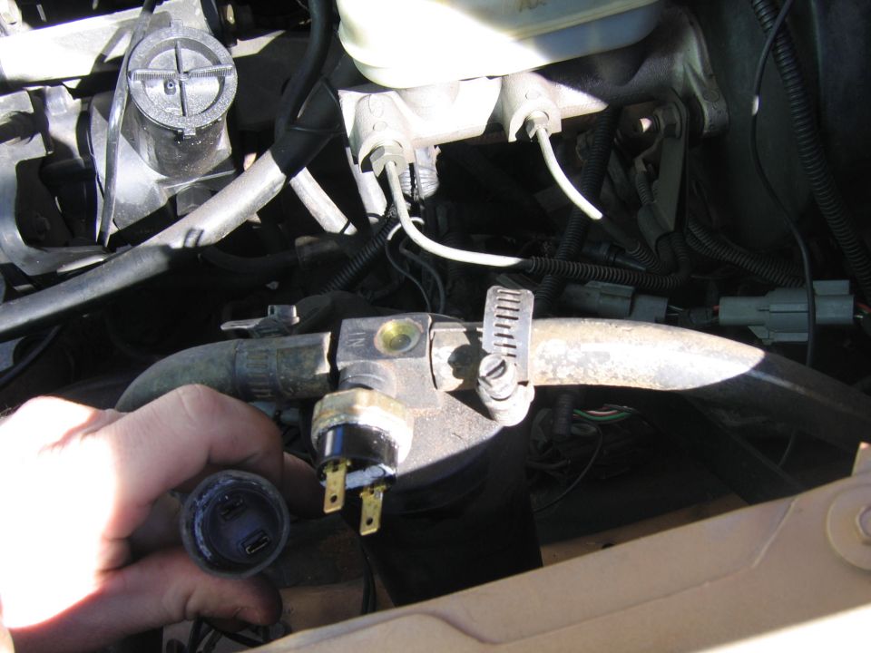 Hand holding a sensor with electrical connectors in an engine bay