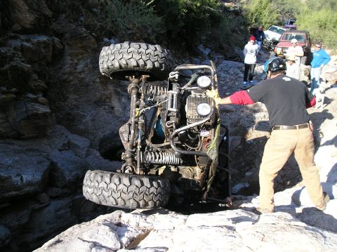 1986 Toyota Hilux - An off-road vehicle has flipped onto its side during an off-road excursion, with onlookers and other vehicles present.