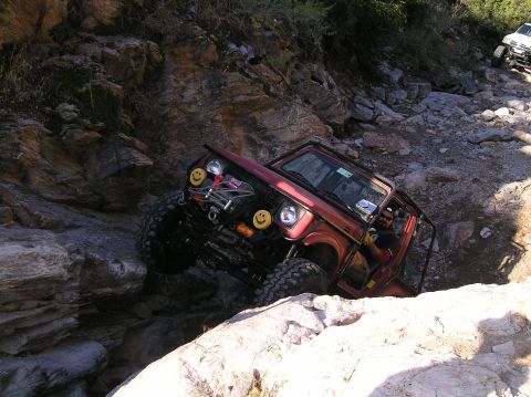 1986 Toyota Hilux - A red off-road vehicle tackles a challenging rocky terrain, with another white vehicle visible in the background.