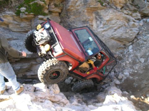 1986 Toyota Hilux - This red off-road vehicle appears to be stuck on a rocky incline, with the driver visible inside.