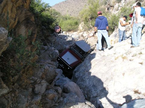 1986 Toyota Hilux - Off-road vehicles navigate a challenging rocky terrain, with one vehicle appearing stuck in a narrow passage.