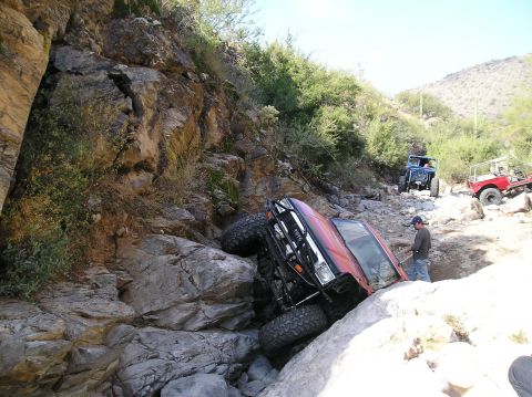 1986 Toyota Hilux - A red 1986 Toyota Hilux is stuck on rocks in a rocky ravine, with two other off-road vehicles in the background.