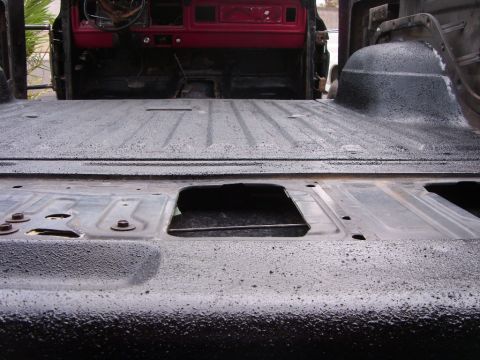 1978 Ford Bronco - Low view across the open tailgate of a gutted SUV, showing the rear floor, wheel tub and tailgate inner panel all sprayed in thick textured…