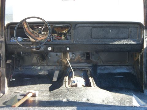 1978 Ford Bronco - Interior of a gutted truck cab shot from behind, with the dash, glovebox door and floor all sprayed in textured black bedliner and the inst…