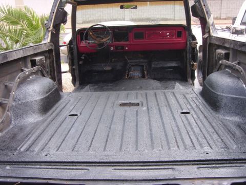 1978 Ford Bronco - Looking forward through the open tailgate of a stripped SUV whose entire rear cargo area, wheel tubs and floor have been sprayed with textu…