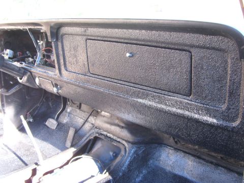 1978 Ford Bronco - The interior of a vehicle shows a textured dashboard with an open glove compartment and exposed wiring.