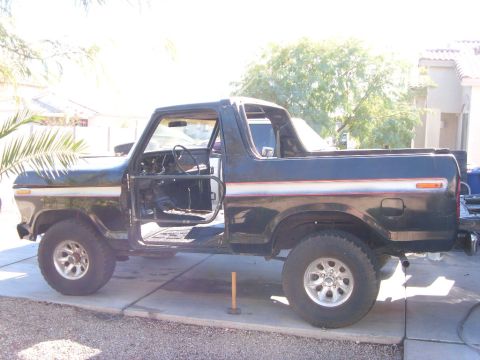 1978 Ford Bronco - Black late-1970s Ford Bronco with doors off and red pinstripe, on a residential driveway in a desert setting.