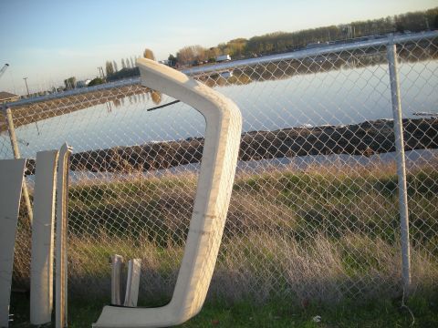 1991 Ford Bronco - Car body trim pieces are stored outdoors near a body of water.