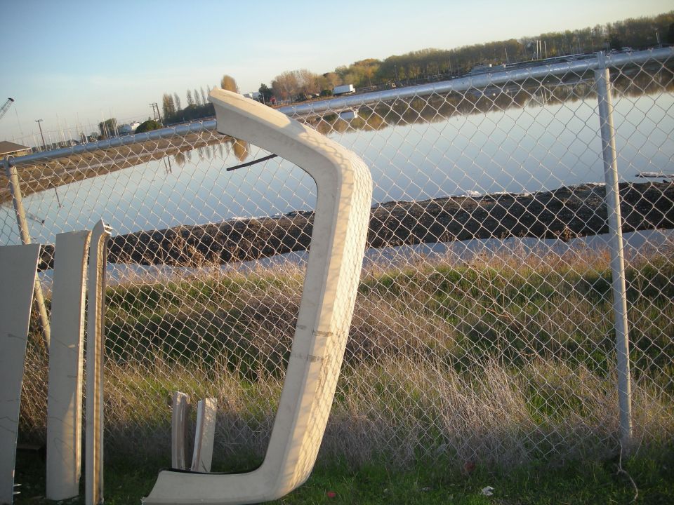 Several beige car body trim pieces leaning against a chain-link fence
