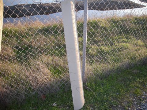 1991 Ford Bronco - A concrete fence post stands near a chain-link fence with overgrown vegetation in the background.
