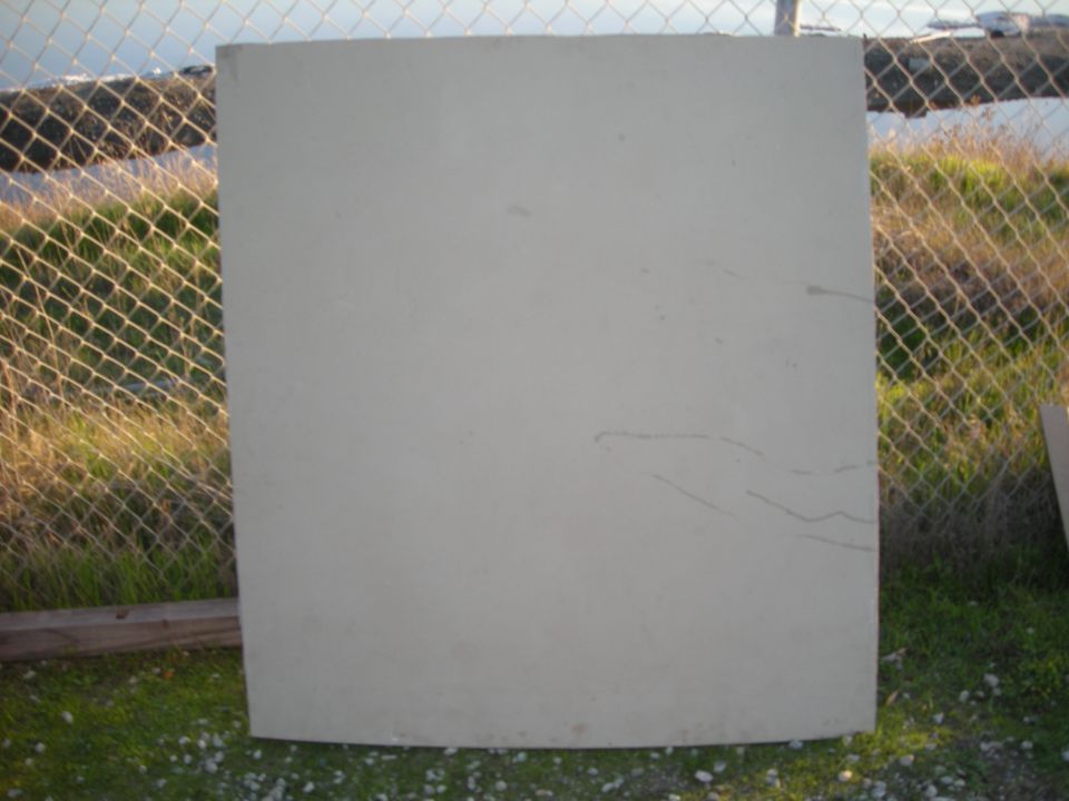 Gray car hood with scratches, outdoors near a chain-link fence