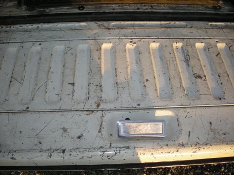 1991 Ford Bronco - Close-up of a white tailgate a chrome handle and textured paneling.