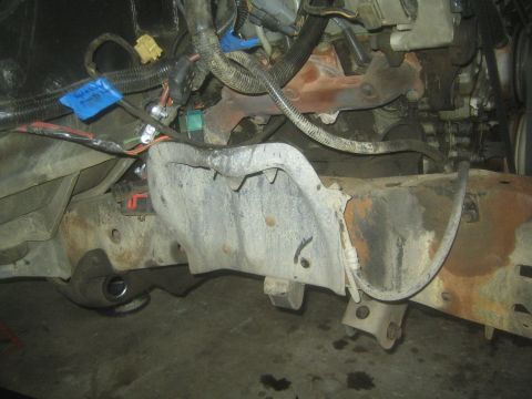 1990 Ford Bronco - Close-up of a rusty truck frame crossmember and wiring harness with blue tape, viewed from beneath the body.