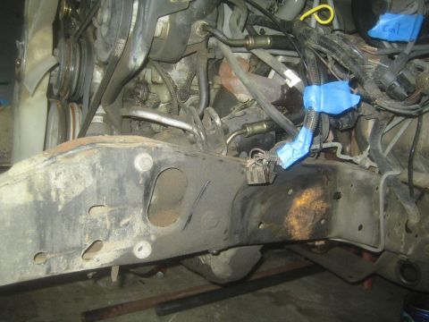 1990 Ford Bronco - Underbody view of a truck frame rail showing blue-taped wiring connectors and engine components above.