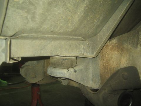 1990 Ford Bronco - Close-up of a truck body mount with rubber bushing beneath the floor pan, supported on a jack stand.