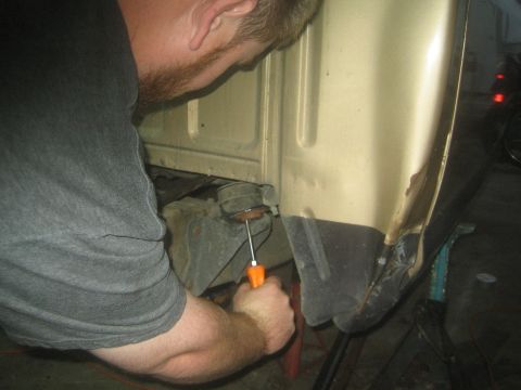 1990 Ford Bronco - man reaches into a gold truck body with an orange-handled screwdriver while working in a dim garage.